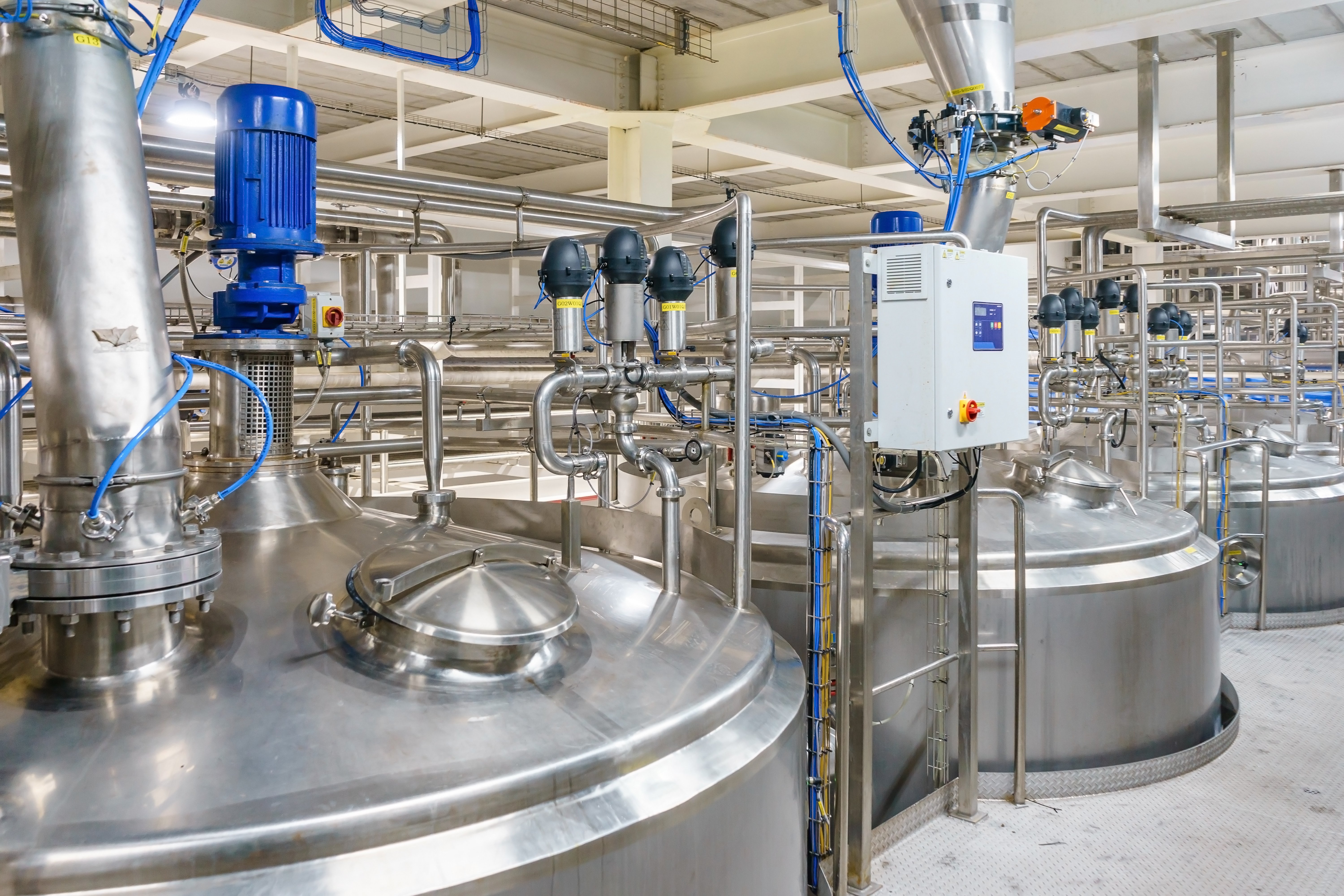 Stainless steel mixing tanks, piping, and processing equipment inside an industrial manufacturing facility.