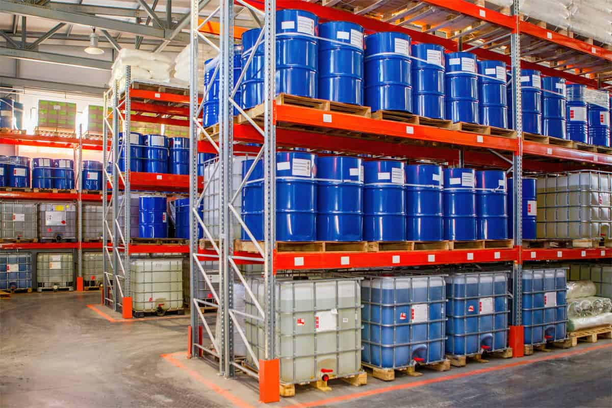 drums and totes filled with liquid chemical products and stacked on shelves in a storage facility